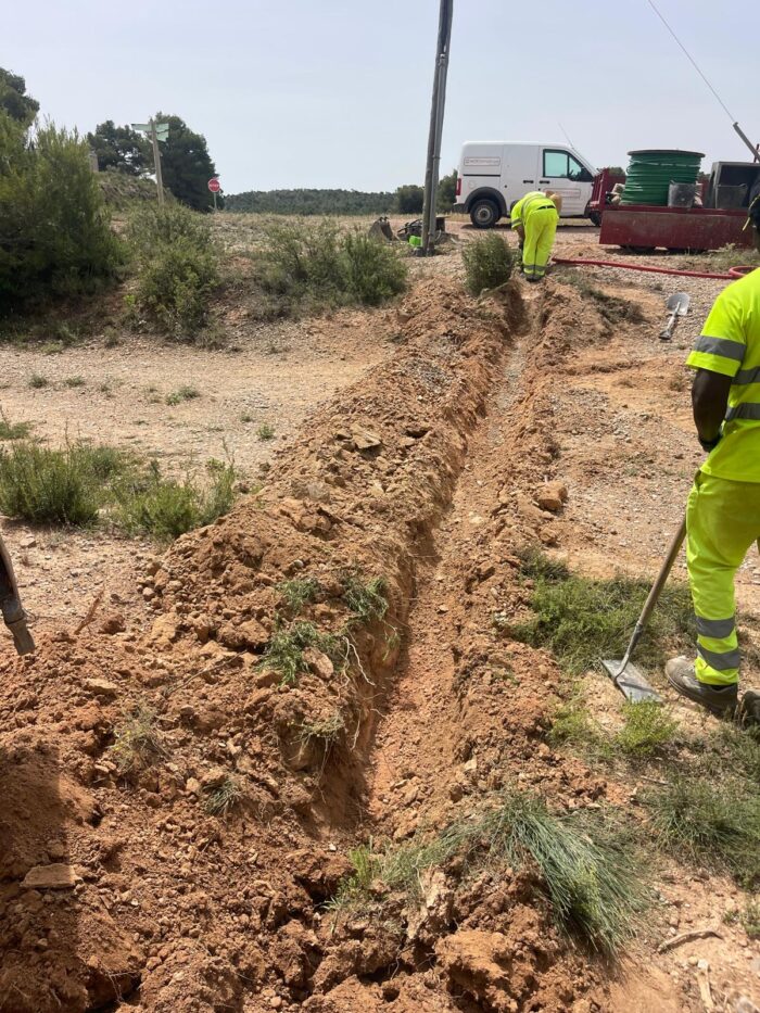 Trabajadores realizando la instalación de fibra óptica en una zanja estrecha en zona rural.